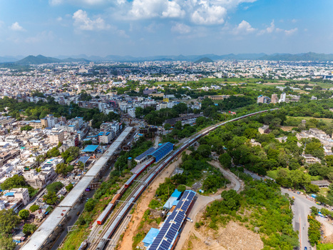 Aerial view of a train traveling on tracks through the urban landscape with solar panels on a nearby building in Udaipur Rajasthan India. Aerial view of a train traveling on tracks through the urban landscape with solar panels on a nearby building in Udaipur Rajasthan India.