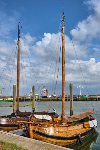Den Oever Netherlands 18 May 2026 View of historic Wieringeraak sailing vessels docked in the fishing harbor under a cloudy blue sky with a wind turbine in the distance. Den Oever Netherlands 18 May 2026 View of historic Wieringeraak sailing vessels docked in the fishing harbor under a cloudy blue sky with a wind turbine in the distance.