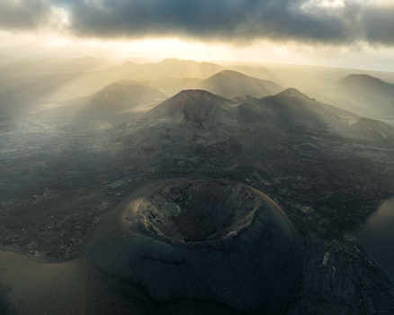 Aerial view of volcanic craters and rugged lava fields under dramatic sunbeams breaking through dark clouds in Lanzarote Canarias Spain. Aerial view of volcanic craters and rugged lava fields under dramatic sunbeams breaking through dark clouds in Lanzarote Canarias Spain.