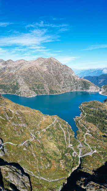 Aerial view of Barrage d Emosson a large dam creating a deep blue reservoir surrounded by rugged alpine mountains winding mountain roads and green slopes in Finhaut Valais Switzerland.