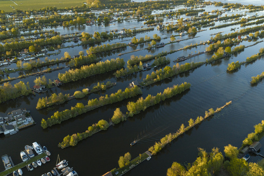 Aerial view of Scheendijk featuring narrow strips of land with lush trees small houses and water channels with a marina filled with boats in Breukelen Utrecht Netherlands. Aerial view of Scheendijk featuring narrow strips of land with lush trees small houses and water channels with a marina filled with boats in Breukelen Utrecht Netherlands.