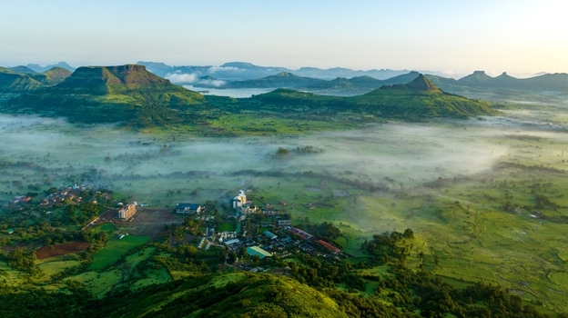 Aerial view of the lush green landscape and rolling hills of the Western Ghats with mist settling over the town of Igatpuri Maharashtra India.