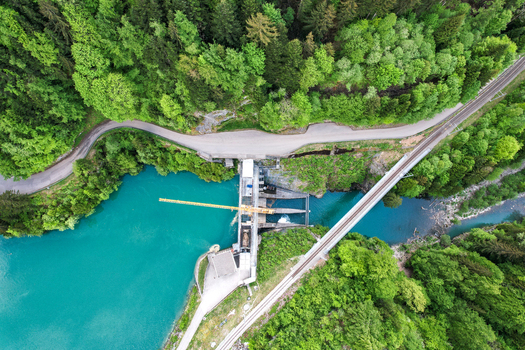 Aerial view of Lac du Vernex dam featuring turquoise water a railway bridge and a winding road through a lush forest Rossiniere Vaud Switzerland.