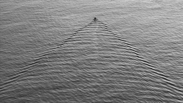 Aerial view of a single solitary boat sits amidst the rippling expanse of the ocean its presence marked by symmetrical waves Carantec Brittany France. Aerial view of a single solitary boat sits amidst the rippling expanse of the ocean its presence marked by symmetrical waves Carantec Brittany France.