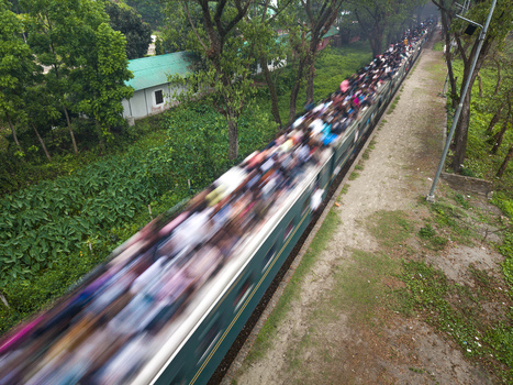 Dhaka Bangladesh 27 March 2026 Aerial view of a train packed with people moving along the tracks a stark contrast to the tranquil greens of the surrounding lush vegetation. Dhaka Bangladesh 27 March 2026 Aerial view of a train packed with people moving along the tracks a stark contrast to the tranquil greens of the surrounding lush vegetation.