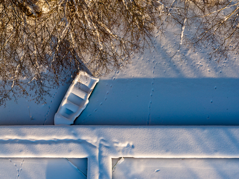 Aerial view of a snow covered boat moored at a frozen pier with animal tracks on the ice and long shadows from bare trees in Trakai Vilnius County Lithuania. Aerial view of a snow covered boat moored at a frozen pier with animal tracks on the ice and long shadows from bare trees in Trakai Vilnius County Lithuania.