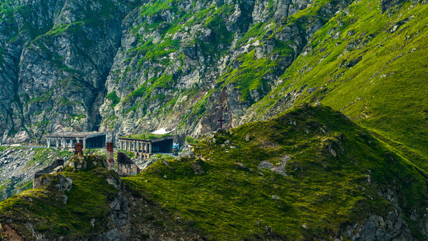 Aerial view of the Transfagarasan mountain pass featuring rugged rocky slopes lush green mountain terrain and concrete tunnel structures in Curtea de Arges Judetul Arges Romania. Aerial view of the Transfagarasan mountain pass featuring rugged rocky slopes lush green mountain terrain and concrete tunnel structures in Curtea de Arges Judetul Arges Romania.