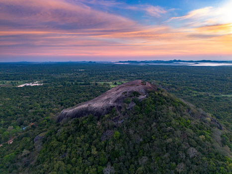 Aerial view of Pidurangala Rock surrounded by dense tropical forest under a vibrant sunset sky in Sigiriya Central Province Sri Lanka. Aerial view of Pidurangala Rock surrounded by dense tropical forest under a vibrant sunset sky in Sigiriya Central Province Sri Lanka.