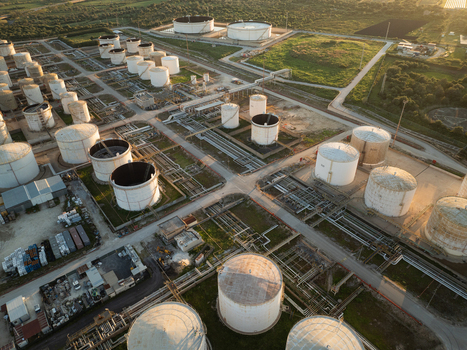 Aerial view of a large industrial oil refinery with numerous white storage tanks and complex piping systems under golden hour light Augusta Sicily Italy. Aerial view of a large industrial oil refinery with numerous white storage tanks and complex piping systems under golden hour light Augusta Sicily Italy.