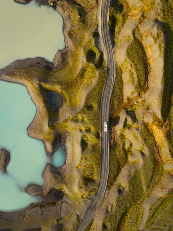 Aerial view of a vehicle driving on a road winding through the mossy terrain near the glacial waters of Breidamerkurjokull Sveitarfelagid Hornafjordur Iceland. Aerial view of a vehicle driving on a road winding through the mossy terrain near the glacial waters of Breidamerkurjokull Sveitarfelagid Hornafjordur Iceland.