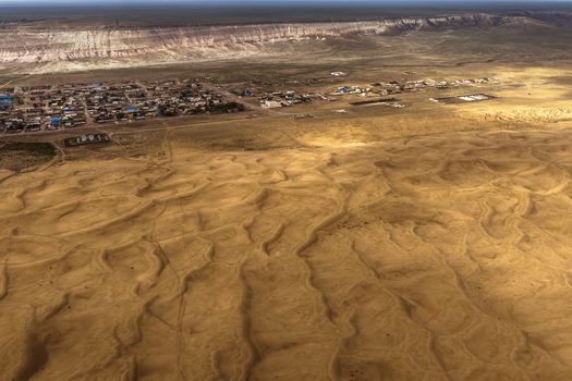 Aerial view of the village of Senek situated next to the vast sand dunes of the desert with a rocky plateau in the background in Senek Mangystau Region Kazakhstan.