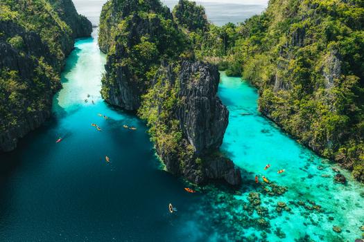 Aerial view of Big Lagoon with turquoise waters limestone cliffs and kayaks paddling through the narrow channel in El Nido Bay Philippines. Aerial view of Big Lagoon with turquoise waters limestone cliffs and kayaks paddling through the narrow channel in El Nido Bay Philippines.