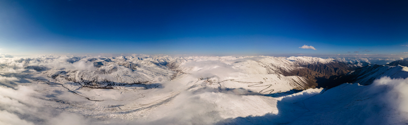 Aerial view of the snow covered Babusar Pass with winding mountain roads and white clouds under a clear blue sky Babusar KPK Pakistan.