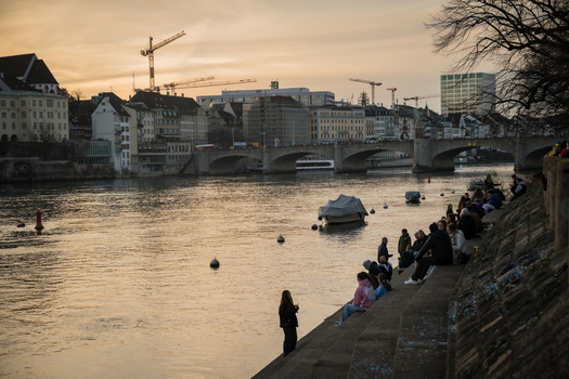 Basel Switzerland 10 March 2025 View of the tranquil Rhine reflecting the soft sunset hues as people gather along the stone embankment near the Mittlere Brücke. Basel Switzerland 10 March 2025 View of the tranquil Rhine reflecting the soft sunset hues as people gather along the stone embankment near the Mittlere Brücke.