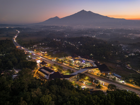 Aerial view of Rest Area Pendopo KM 456 B illuminated at twilight with the Trans Java Toll Road and Mount Merbabu in the background in Pabelan Central Java Indonesia.