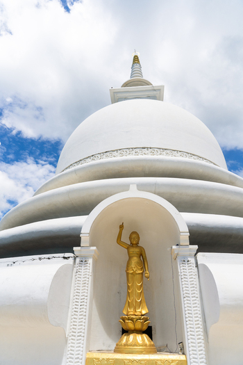 View of the Japanese Peace Pagoda Rumassala featuring a golden Buddha statue in a white niche against a blue sky with clouds in Unawatuna Southern Province Sri Lanka. View of the Japanese Peace Pagoda Rumassala featuring a golden Buddha statue in a white niche against a blue sky with clouds in Unawatuna Southern Province Sri Lanka.