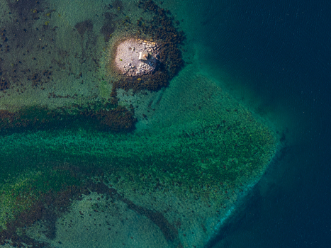Aerial view of a small rocky islet with a structure surrounded by clear turquoise and deep blue fjord waters in Geiranger More og Romsdal Norway. Aerial view of a small rocky islet with a structure surrounded by clear turquoise and deep blue fjord waters in Geiranger More og Romsdal Norway.
