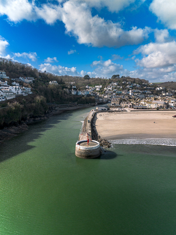 Aerial view of the harbor and beach featuring the stone pier calm green water and the town nestled on the hillside in Looe Cornwall United Kingdom. Aerial view of the harbor and beach featuring the stone pier calm green water and the town nestled on the hillside in Looe Cornwall United Kingdom.