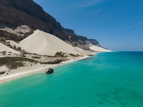 Aerial view of turquoise waters caress the shore contrasting with stark white dunes nestled against rugged cliffs creating a stunning coastal panorama Erissel Socotra Yemen.