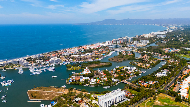 Aerial view of where the sapphire sea meets the sandy shore cradling buildings and boats in a vibrant dance of blue and beige Nuevo Vallarta Mexico.