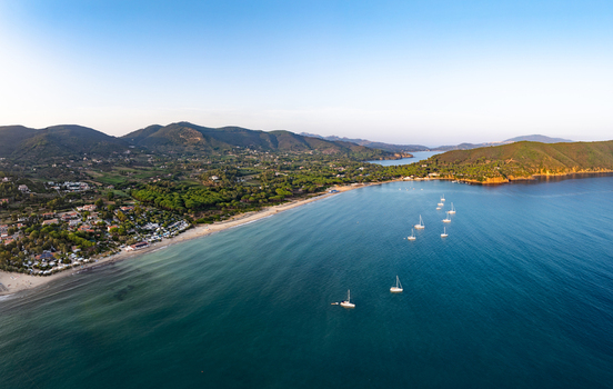Aerial view of sailboats in Lacona Bay with a sandy beach lush green hills and clear blue water in Lacona Tuscany Italy.