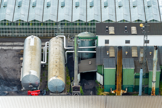 Aerial view of greenhouse climate control installations featuring large industrial storage tanks adjacent glass greenhouse structures in Poland. Aerial view of greenhouse climate control installations featuring large industrial storage tanks adjacent glass greenhouse structures in Poland.