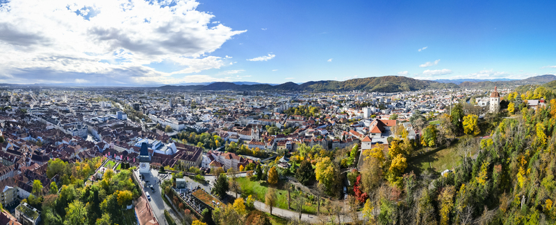 Aerial view of the city s rooftops and autumn colored trees nestled between hills and under a bright sky Graz Styria Austria.