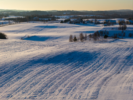 Aerial view of snow covered rolling hills and rural houses under a soft golden sunset light Lithuania. Aerial view of snow covered rolling hills and rural houses under a soft golden sunset light Lithuania.