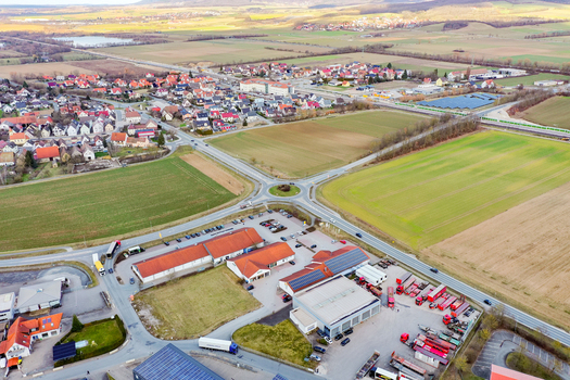 Aerial view of Buttenheim showing a roundabout commercial buildings with parked trucks and vast agricultural fields under a clear sky in Buttenheim Bavaria Germany. Aerial view of Buttenheim showing a roundabout commercial buildings with parked trucks and vast agricultural fields under a clear sky in Buttenheim Bavaria Germany.