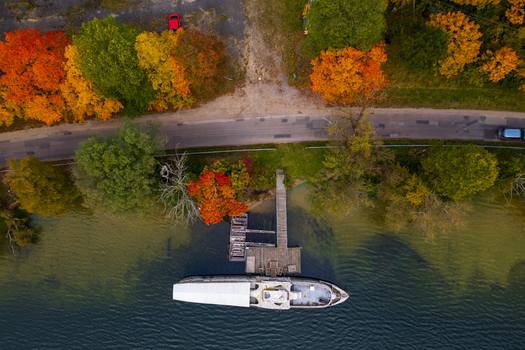 Aerial view of a boat moored at a wooden pier on the lake shore surrounded by vibrant autumn trees and a road in Trakai Vilnius County Lithuania. Aerial view of a boat moored at a wooden pier on the lake shore surrounded by vibrant autumn trees and a road in Trakai Vilnius County Lithuania.
