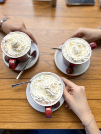 View of three mugs of hot chocolate topped with whipped cream on a wooden table with hands of people Beylikduzu Istanbul Turkiye. View of three mugs of hot chocolate topped with whipped cream on a wooden table with hands of people Beylikduzu Istanbul Turkiye.