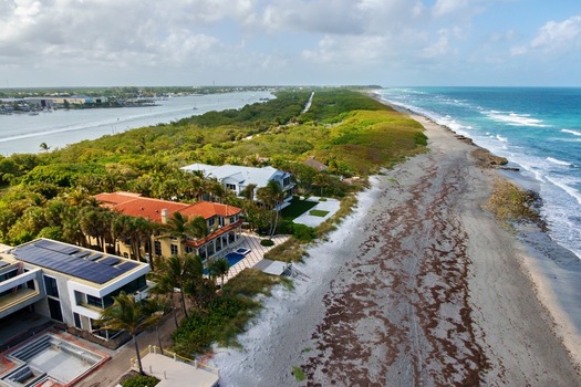 Aerial view of the coastline where the deep blue sea meets the sandy shore lush green vegetation thrives and houses stand elegantly Jupiter Island Florida United States. Aerial view of the coastline where the deep blue sea meets the sandy shore lush green vegetation thrives and houses stand elegantly Jupiter Island Florida United States.