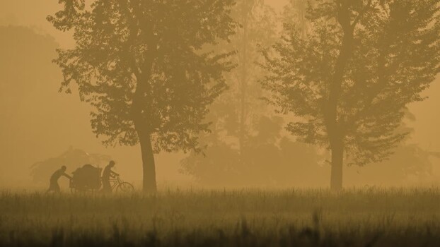 View of people pushing a cart through misty fields Bangladesh.