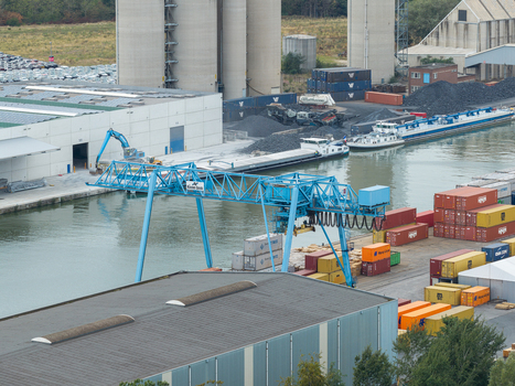 Genk Belgium 27 August 2026 Aerial view of Kolenhaven industrial port with a blue gantry crane container terminal inland shipping barges and warehouses along the canal.