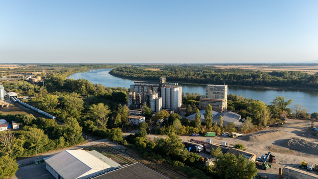 Aerial view of the industrial grain silos and storage facility situated along the Sava River surrounded by lush trees and railway tracks in Sremska Mitrovica Vojvodina Serbia. Aerial view of the industrial grain silos and storage facility situated along the Sava River surrounded by lush trees and railway tracks in Sremska Mitrovica Vojvodina Serbia.