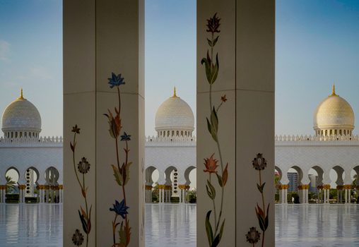 View of the ornate white marble columns with floral patterns and the majestic domes of a grand mosque under a clear sky in Abu Dhabi Abu Dhabi United Arab Emirates. View of the ornate white marble columns with floral patterns and the majestic domes of a grand mosque under a clear sky in Abu Dhabi Abu Dhabi United Arab Emirates.