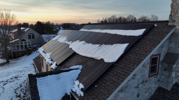 Aerial view of solar panels on a residential roof partially covered in snow during a golden hour sunset in Warwick Township Pennsylvania United States.