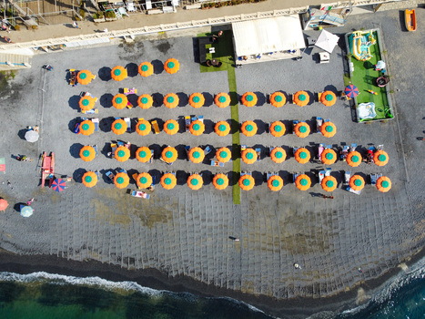 Aerial view of organized rows of colorful beach umbrellas on a pebble shore with clear turquoise water in Imperia Liguria Italy. Aerial view of organized rows of colorful beach umbrellas on a pebble shore with clear turquoise water in Imperia Liguria Italy.