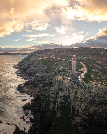 Aerial view of Faro de Punta Nariga lighthouse on a rugged rocky cliff with crashing waves and golden sunset light Malpica A Coruna Spain. Aerial view of Faro de Punta Nariga lighthouse on a rugged rocky cliff with crashing waves and golden sunset light Malpica A Coruna Spain.