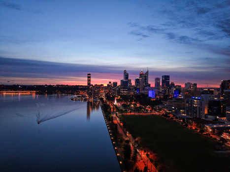 Aerial view of the Perth skyline illuminated at twilight along the Swan River with a boat leaving a wake in City of Perth Western Australia Australia.