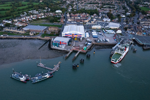 Aerial view of the Wight Shipyard Co with its distinctive Union Jack roof featuring a ferry docked at the pier and smaller vessels at the jetty in Cowes England United Kingdom.