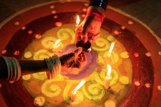 View of hands lighting traditional clay lamps on a vibrant rangoli pattern during Diwali celebrations in Rahim Yar Khan Punjab Pakistan.
