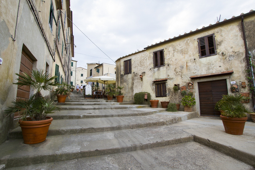 View of weathered buildings flank a stepped street lined with potted plants leading to a sunlit terrace Portoferraio Tuscany Italy.