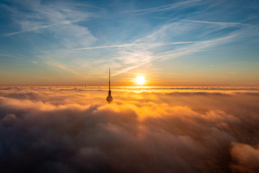 Aerial view of the Berlin TV Tower poking through a sea of clouds during a golden sunset in Berlin Berlin Germany.