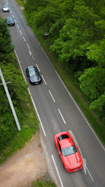 Aerial view of a red sports car and other vehicles driving along a paved road surrounded by dense green trees La Chapelle de Guinchay Bourgogne Franche Comte France.