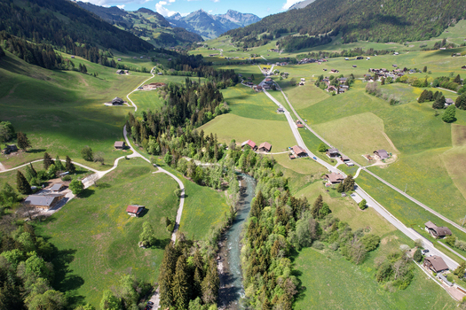 Aerial view of the village of Rougemont featuring traditional chalets a flowing river and lush green alpine pastures under a blue sky Rougemont Vaud Switzerland. Aerial view of the village of Rougemont featuring traditional chalets a flowing river and lush green alpine pastures under a blue sky Rougemont Vaud Switzerland.