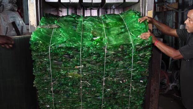 View of a man processing a bale of green plastic bottles Bangladesh. View of a man processing a bale of green plastic bottles Bangladesh.