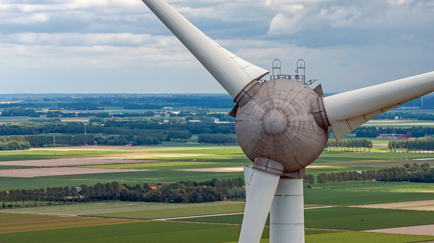 Aerial view of a wind turbine hub and blades set against a backdrop of green and brown agricultural fields in the flat landscape of the Flevoland province Rutten Flevoland Netherlands. Aerial view of a wind turbine hub and blades set against a backdrop of green and brown agricultural fields in the flat landscape of the Flevoland province Rutten Flevoland Netherlands.