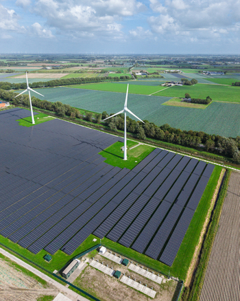 Aerial view of a large solar farm integrated with wind turbines in a rural landscape with green fields and blue sky in Warmenhuizen North Holland Netherlands.