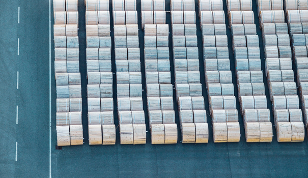 Aerial view of rows of large wooden cable reels arranged in an industrial yard creating a repetitive pattern linked to logistics and electrical infrastructure in Italy. Aerial view of rows of large wooden cable reels arranged in an industrial yard creating a repetitive pattern linked to logistics and electrical infrastructure in Italy.